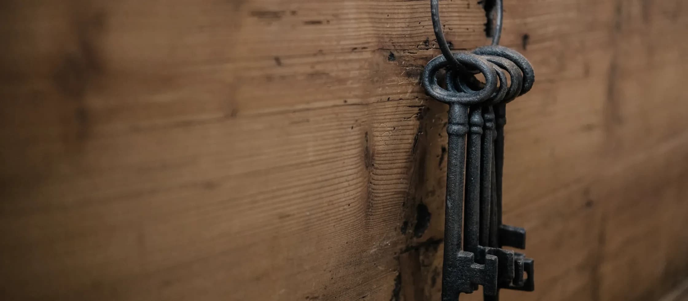 Two iron keys hanging from a ring on a nail driven into a timber wall.